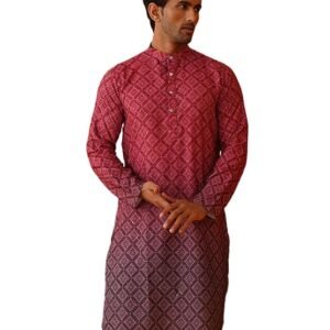 "A male model standing with legs crossed, wearing a long-sleeved ethnic kurta that features a color gradient fading from maroon at the top to deep purple at the bottom. The kurta has an all-over geometric diamond pattern. He is wearing crisp white straight-cut trousers and black slip-on ethnic shoes. He stands against a backdrop of a bright red wall with a traditional scalloped archway and a wooden cane bench."